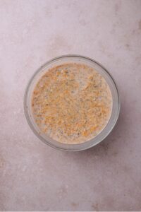 A glass bowl filled with oats, pumpkin, and chia seeds soaking in milk.