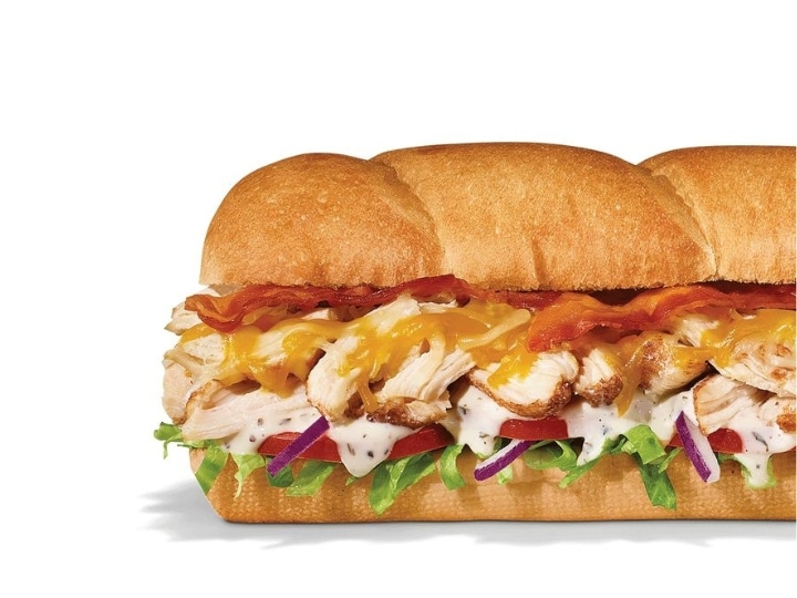 Part of a sub with bacon, chicken, ranch, cheese, lettuce, tomato, and onion.