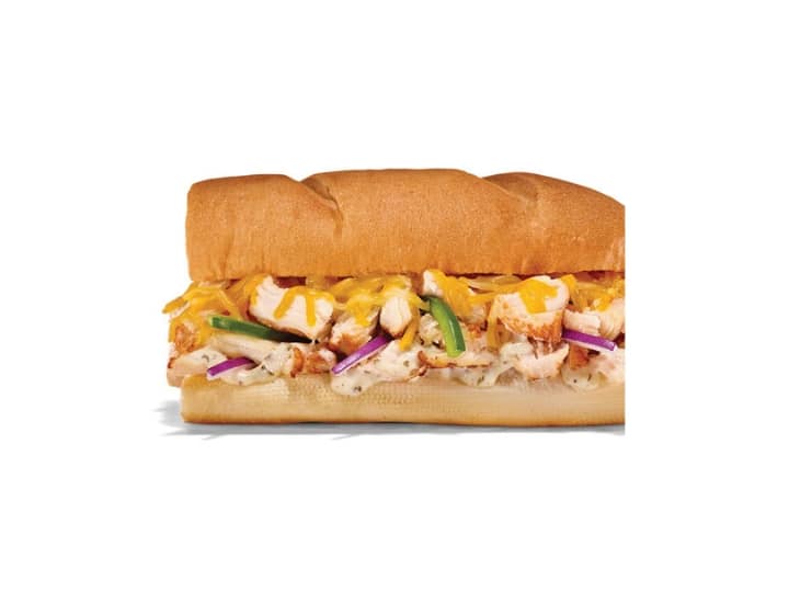 A sub with shredded cheese, green pepper, red onion, and chicken.