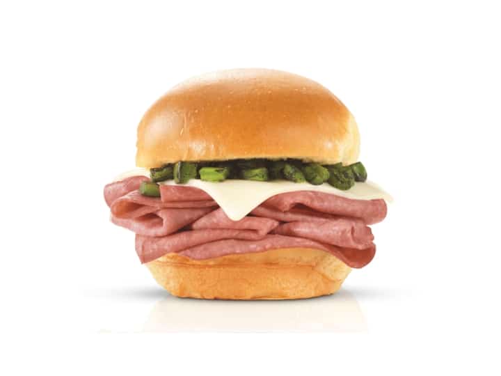 A bun with diced jalapeno, cheese, and roast beef between it.