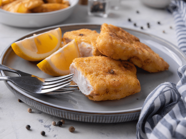 A piece of fried breaded grouper cut in half on a grey plate.