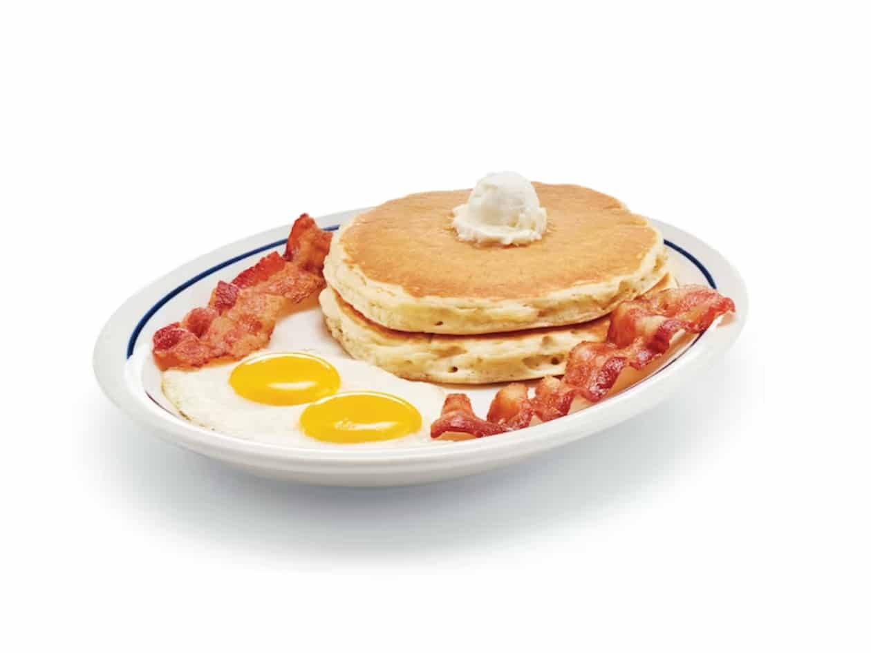 A stack of two pancakes, two slices of bacon, and two sunny side up eggs on a plate.