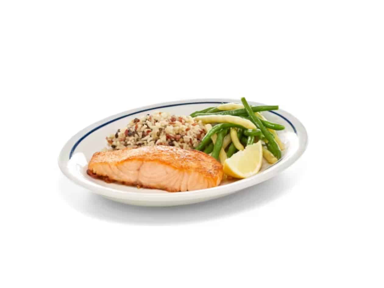 A piece of salmon, rice, and green beans on a white plate.