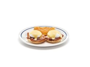 Two poached eggs on top of ham on biscuits on a white plate.