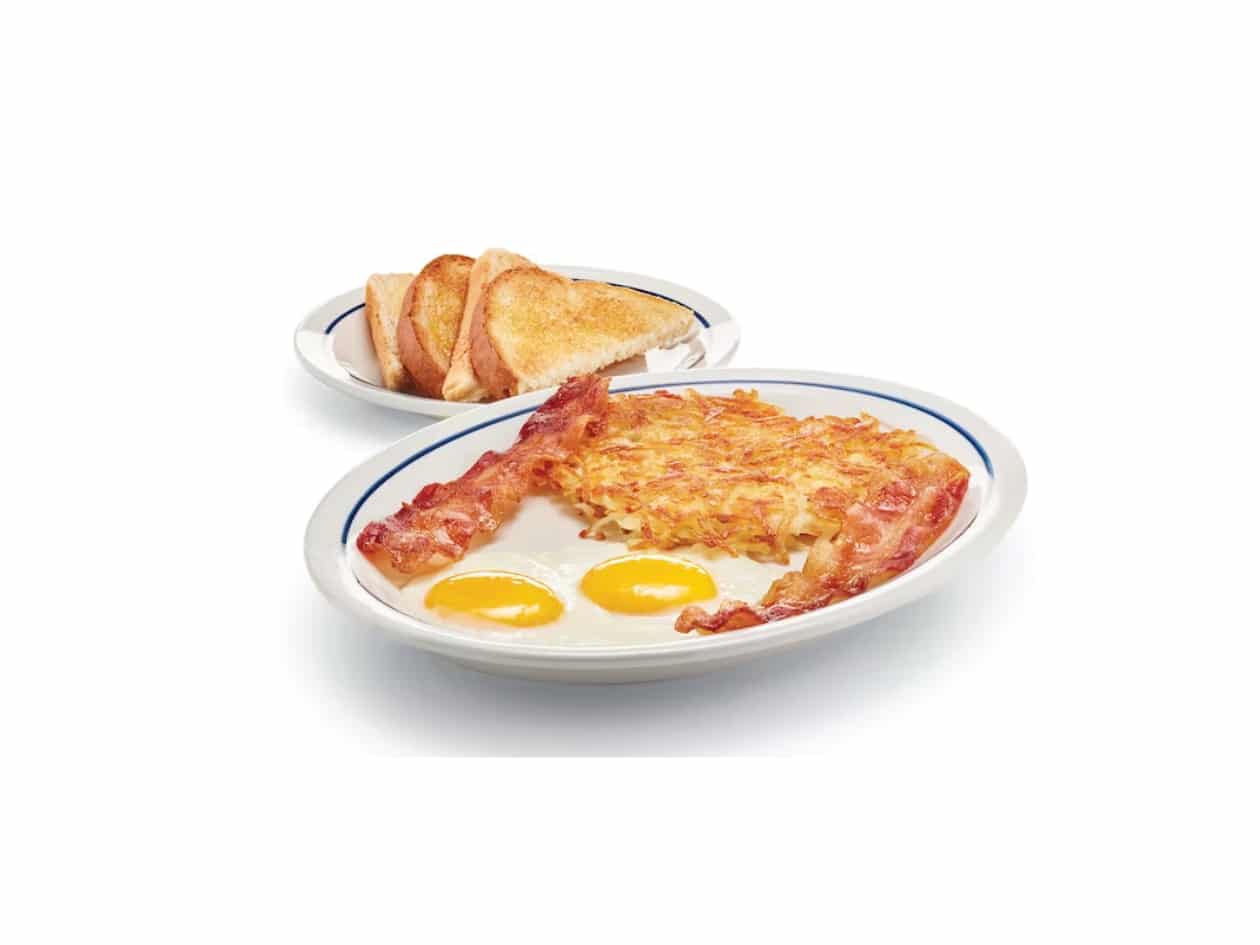 Two eggs, bacon, and hashbrowns on a white plate. Behind it is four slices of toast.