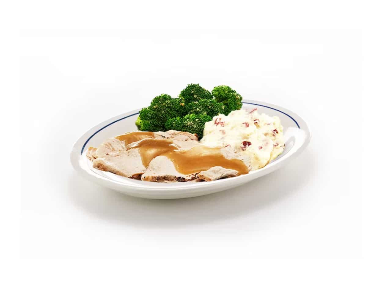 A few slices of turkey with gravy on top, mashed potatoes, and broccoli on a white plate.