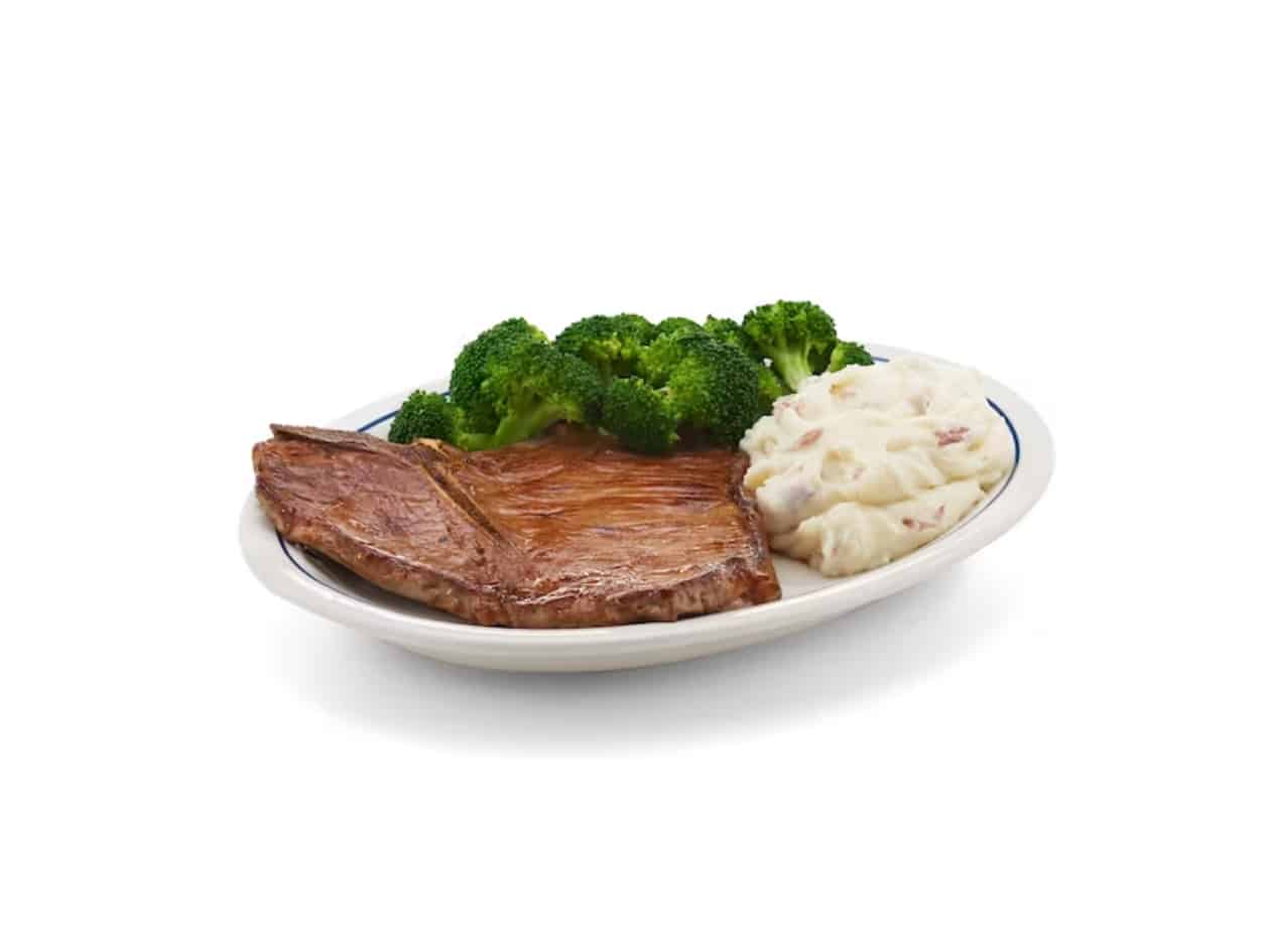 A t bone steak, broccoli, and mashed potatoes on a white plate.