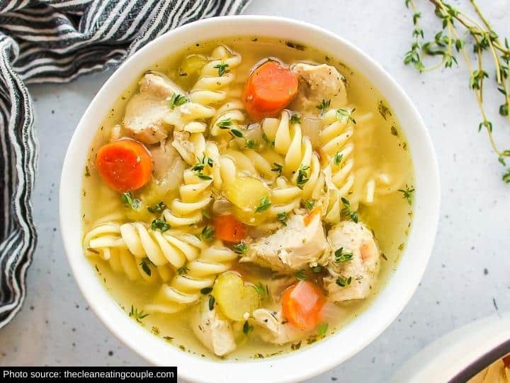 Spiral noodles, carrots, and chicken in broth in a white bowl on a white counter.