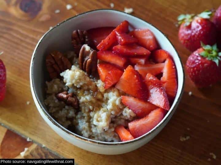 Sliced strawberries, pecans, and steel cut oatmeal in a white bowl on a wood cutting board.