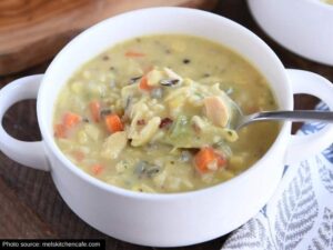 A spoon with creamy chicken wild rice soup on it in a white bowl.