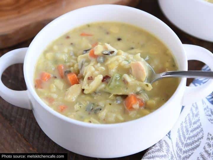 A spoon with creamy chicken wild rice soup on it in a white bowl.