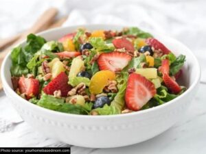 Sliced strawberries, mandarin oranges, blueberries, and lettuce in a white bowl.