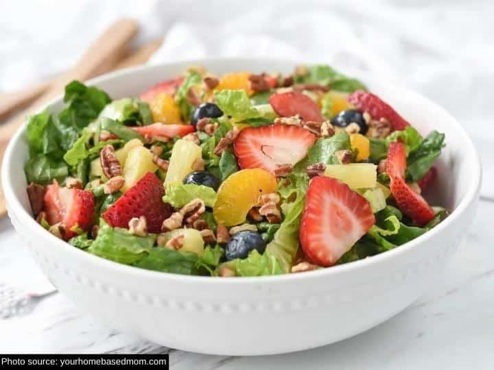 Sliced strawberries, mandarin oranges, blueberries, and lettuce in a white bowl.