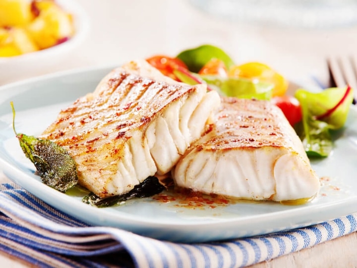 Two pieces of cooked pollock on top of one another on a white plate.