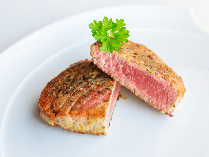 Two pieces of cooked tuna leaned against one another on a white plate.