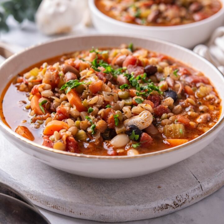 A bowl of bean soup in a ceramic soup bowl on a wooden serving board. There is another bowl of soup in the background.