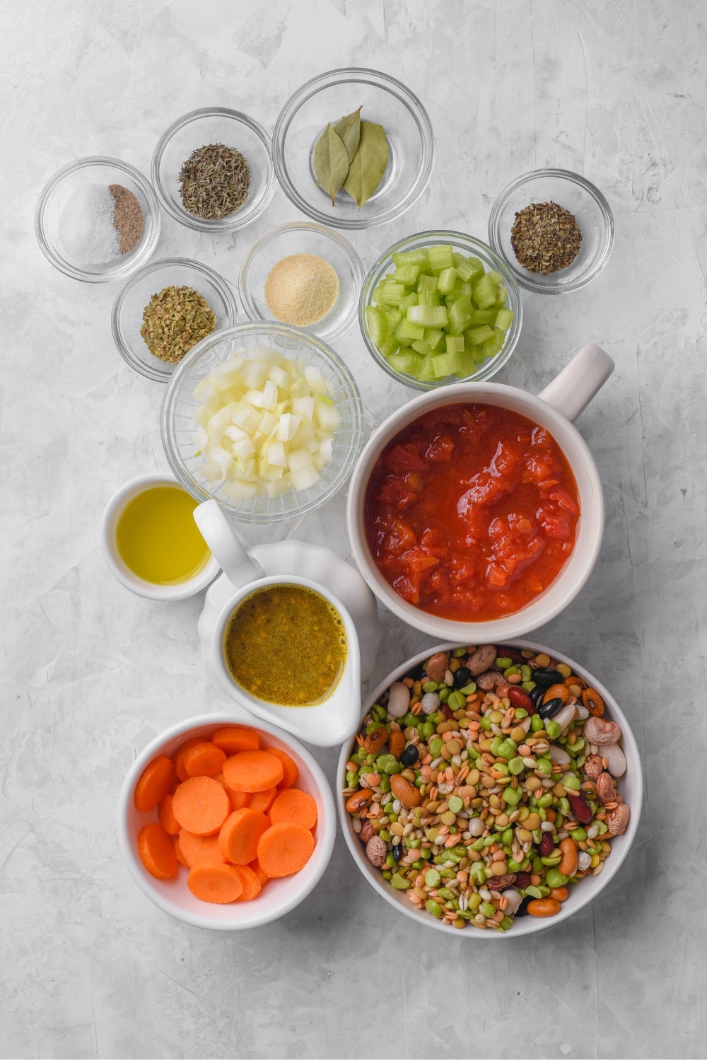 Glass bowls in various sizes filled with different ingredients including beans, canned tomatoes, carrots, onion, celery, and seasonings.