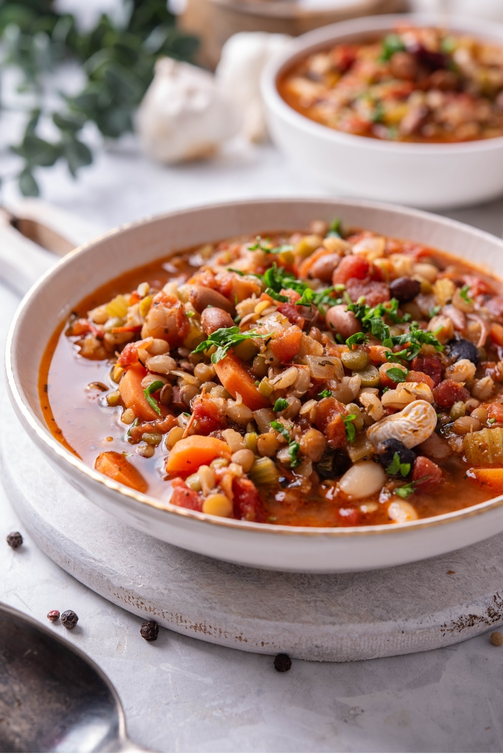 A bowl of bean soup in a ceramic soup bowl on a wooden serving board. There is another bowl of soup in the background.