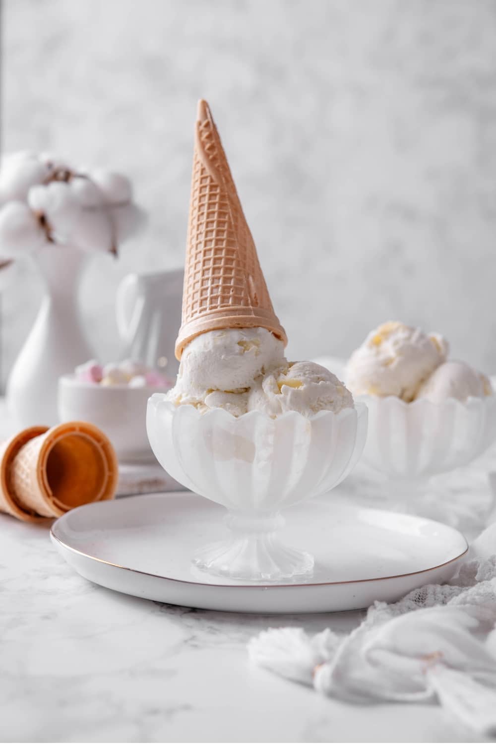 Three scoops of vanilla protein ice cream in a glass sundae bowl with a cone on top.