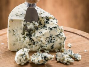 A block of blue cheese with a knife in it and some crumbles in front of it.
