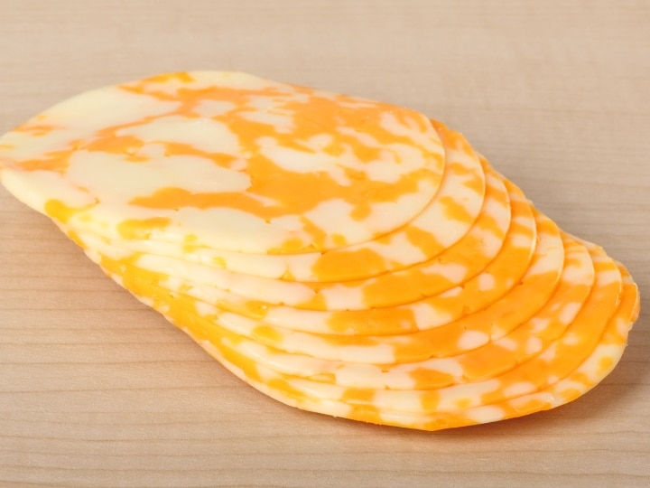 A bunch of slices of colby cheese on a wood table.