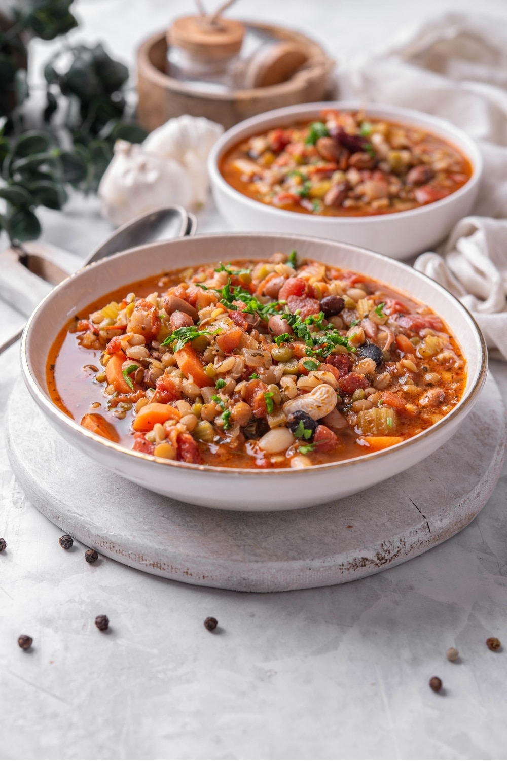 A bowl of bean soup in a ceramic soup bowl on a wooden serving board. There is another bowl of soup in the background.