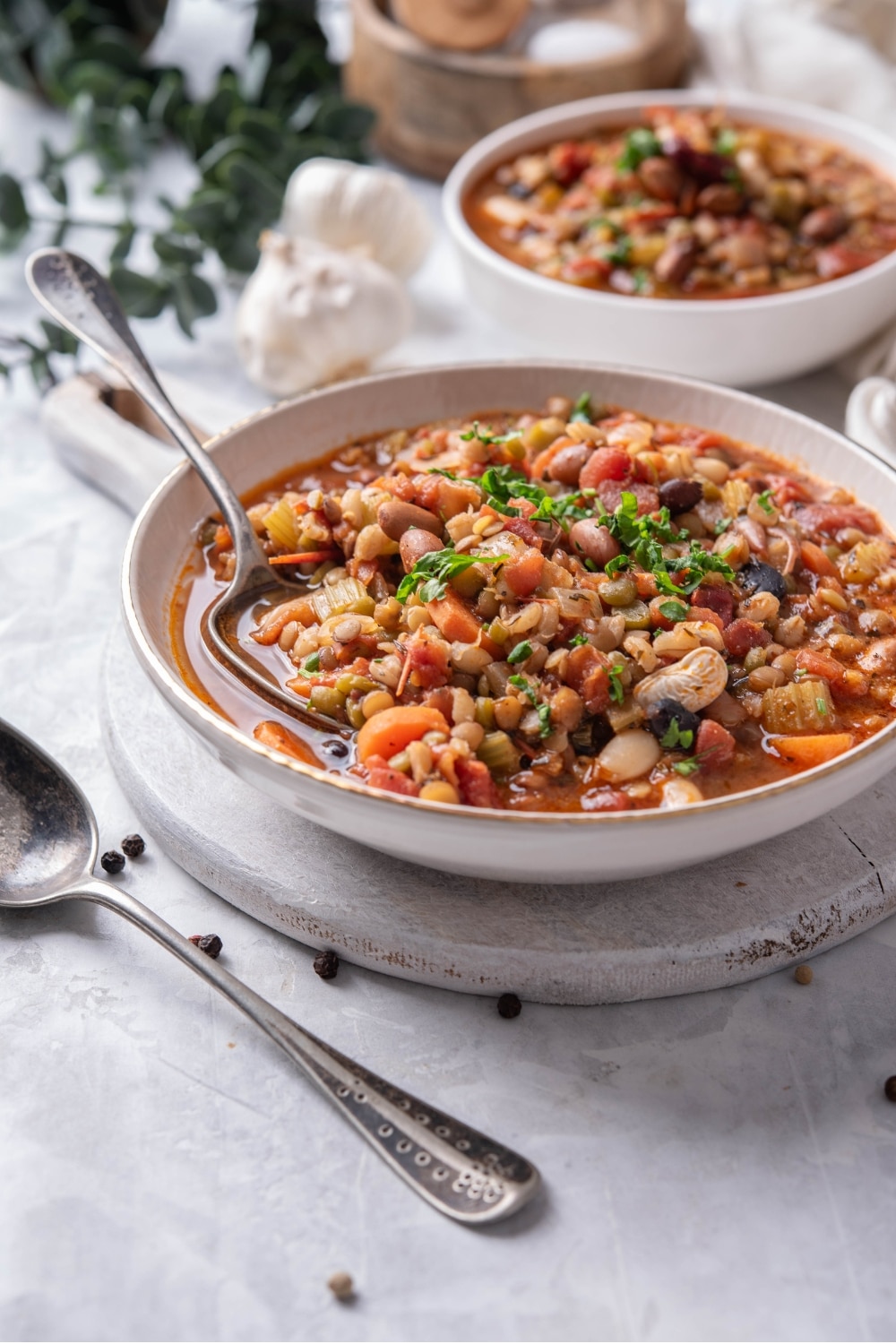 A bowl of bean soup in a ceramic soup bowl on a wooden serving board. There is a spoon dipped in the soup with another bowl of soup in the background.