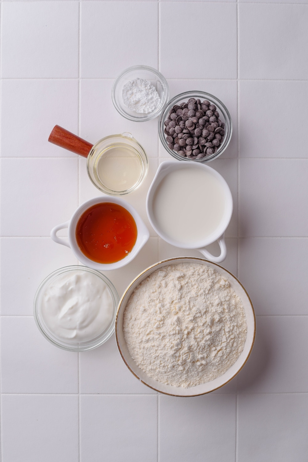 An overhead shot of various glass bowls holding different ingredients including flour, coconut milk, syrup, coconut cream, and chocolate chips.