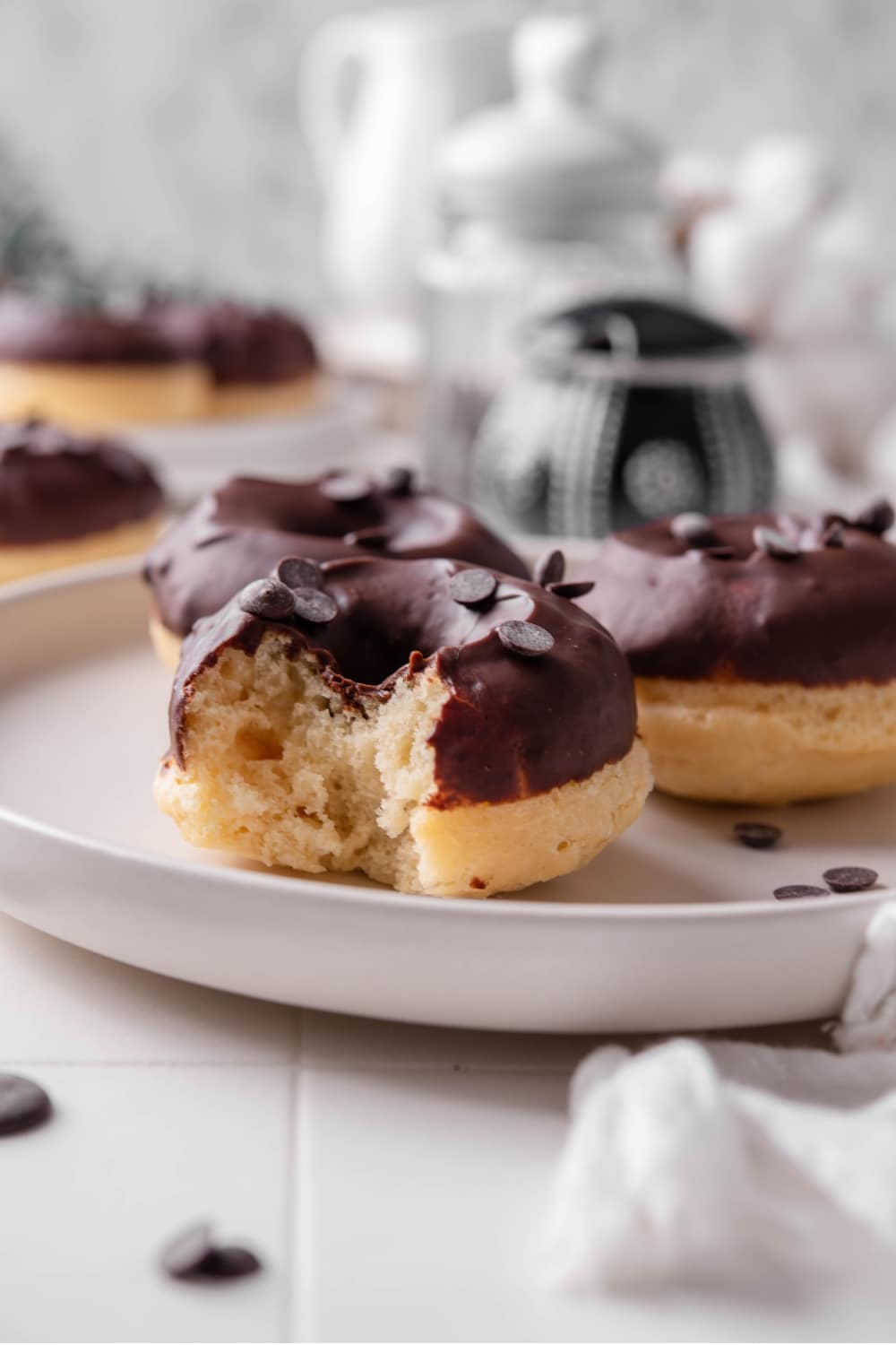 A ceramic plate with three baked donuts with chocolate frosting on top. The donuts are sprinkled with chocolate chips and one of the donuts has a bite taken out of it.