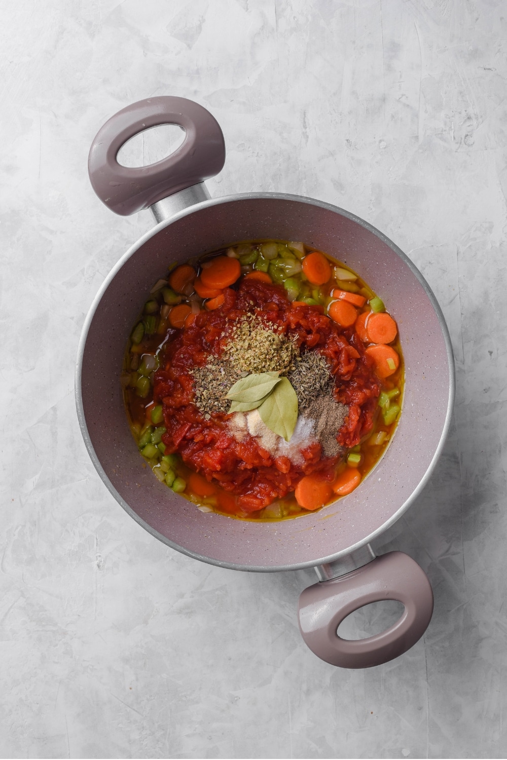 An overhead shot of a large stock pot filled with broth, vegetables, and seasonings.