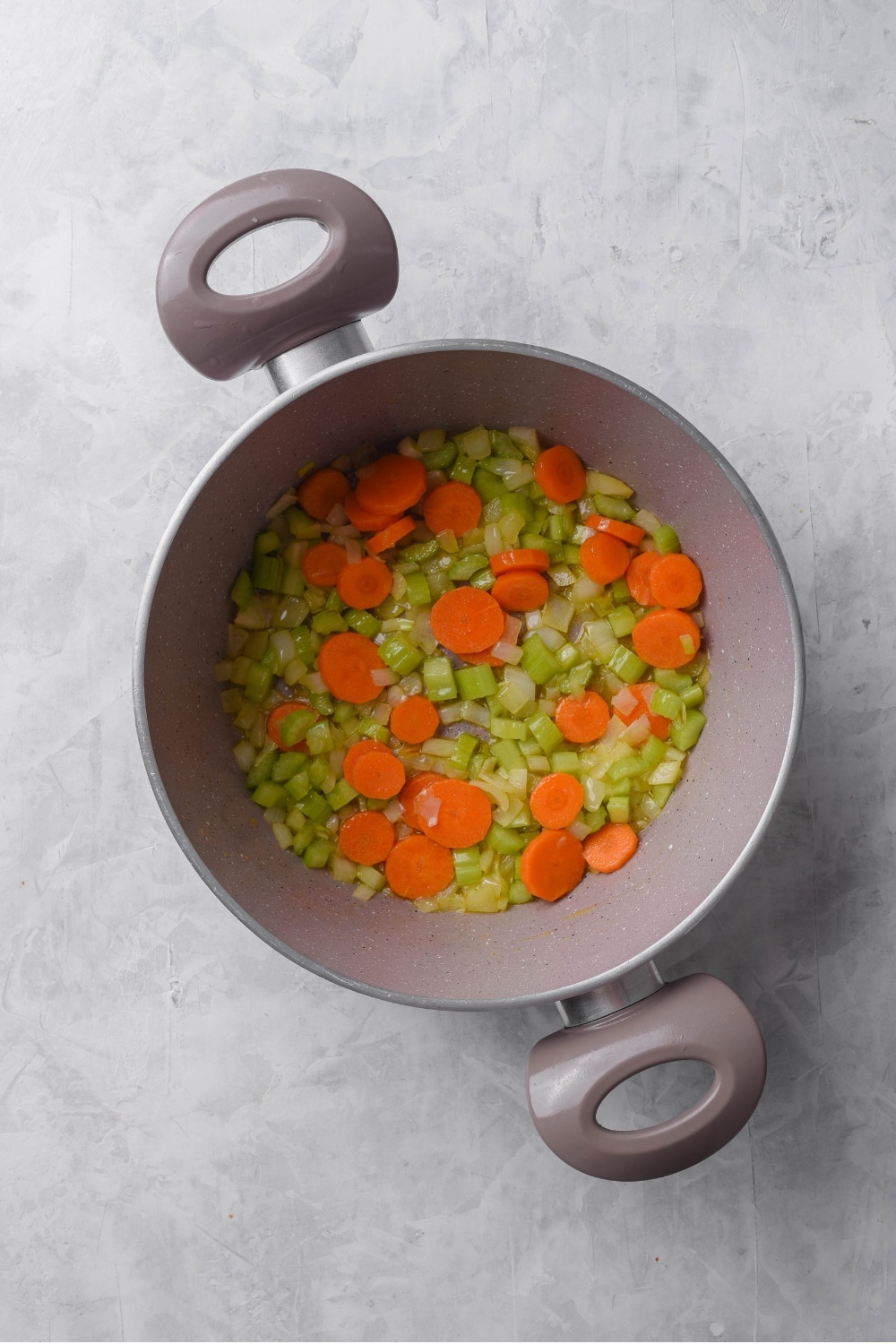 An overhead shot of a large stock pot filled with carrots, celery, and onion.