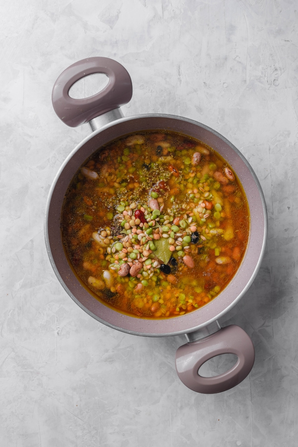 An overhead shot of a large stock pot filled with broth, vegetables, seasonings, and beans on top.