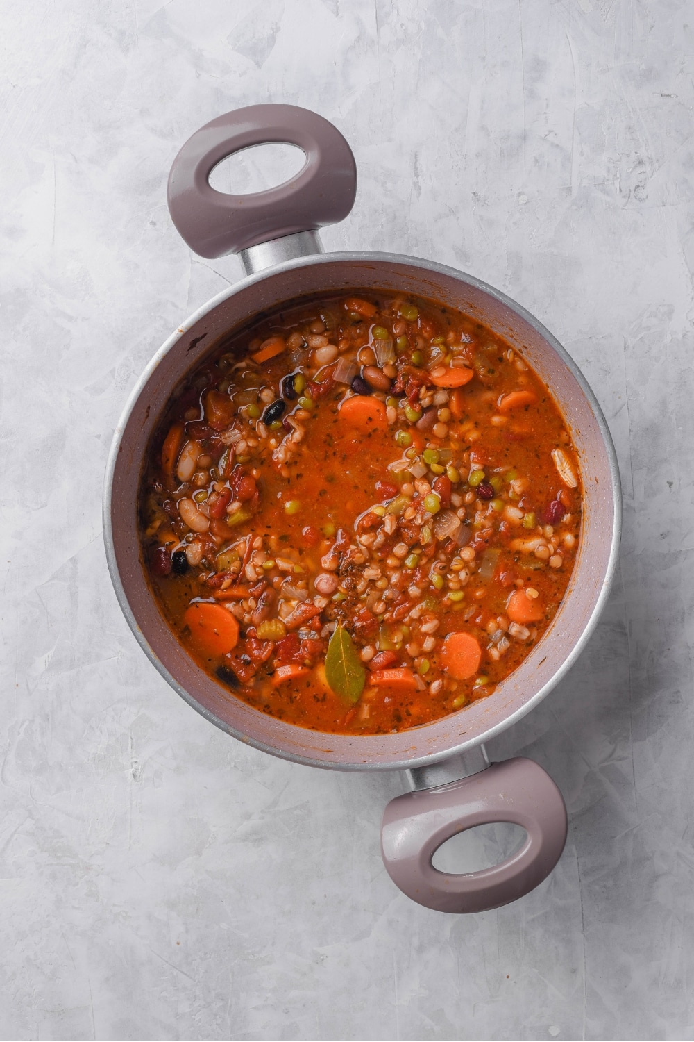 An overhead shot of a large stock pot filled with bean soup including a vegetable broth, carrots, and beans on top.