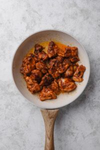 An overhead shot of a ceramic skillet with pieces of chicken cooking in an al pastor marinade sauce.