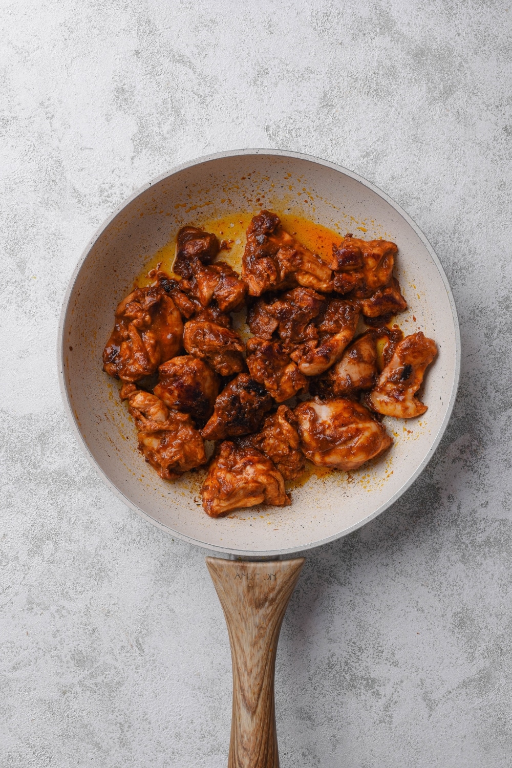 An overhead shot of a ceramic skillet with pieces of chicken cooking in an al pastor marinade sauce.