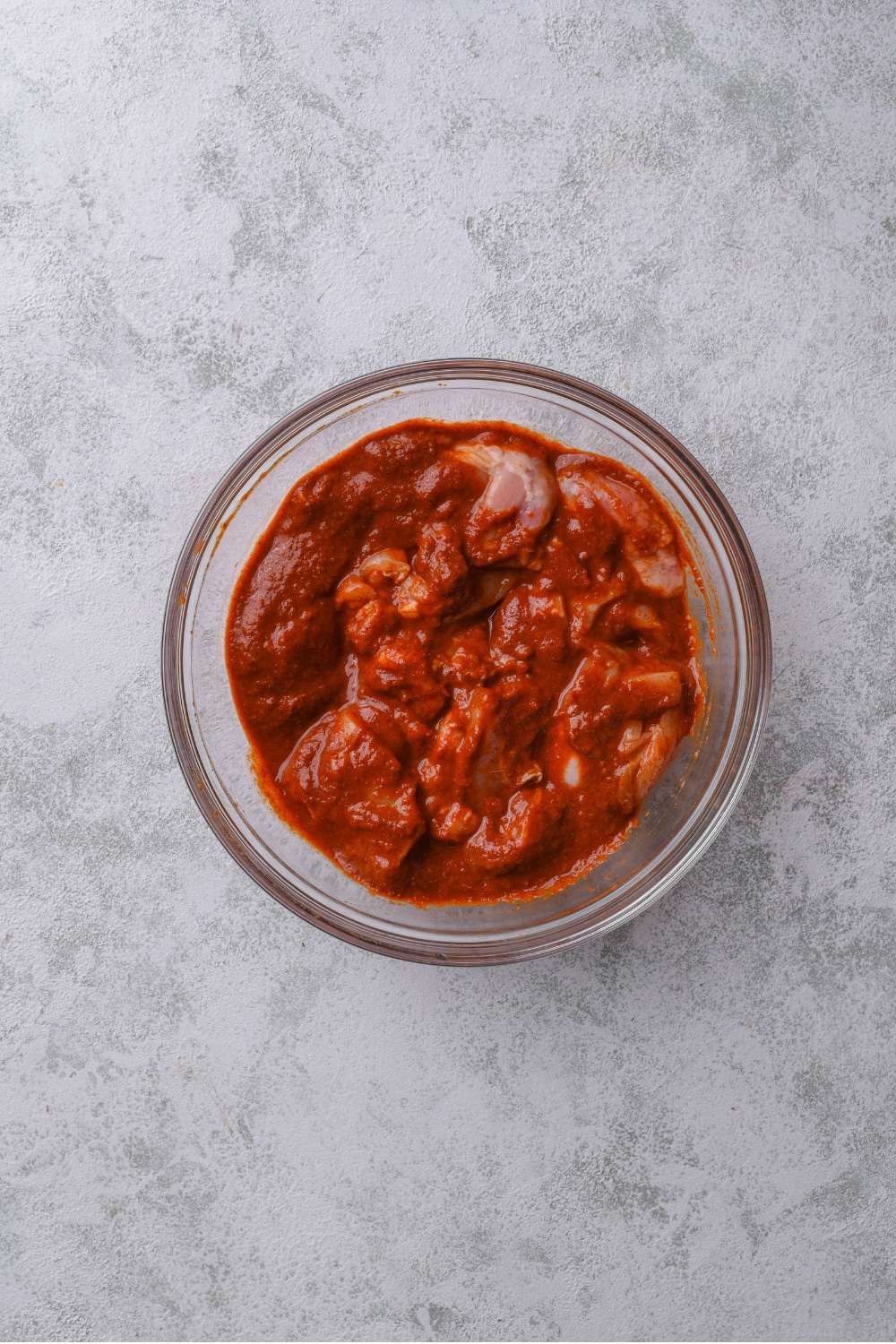 An overhead shot of a glass bowl with chicken thighs marinating in an al pastor sauce.