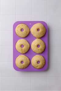 A silicone donut pan with six baked donuts on a tiled counter.