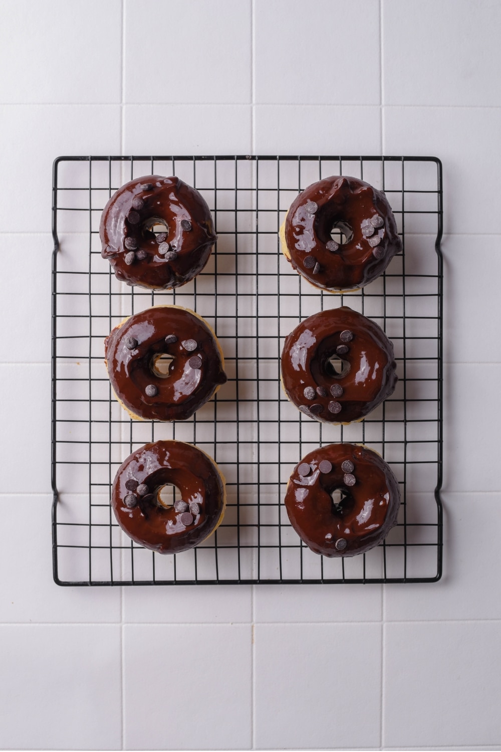 A wire rack with six baked donuts dipped in chocolate with chocolate chips on top.