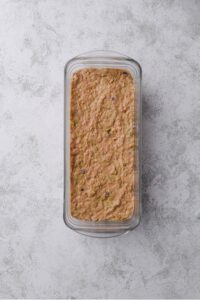 A glass loaf pan with raw zucchini bread batter.