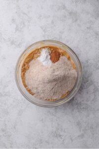 A glass bowl filled with zucchini bread batter with flour, cinnamon, and baking soda on top.