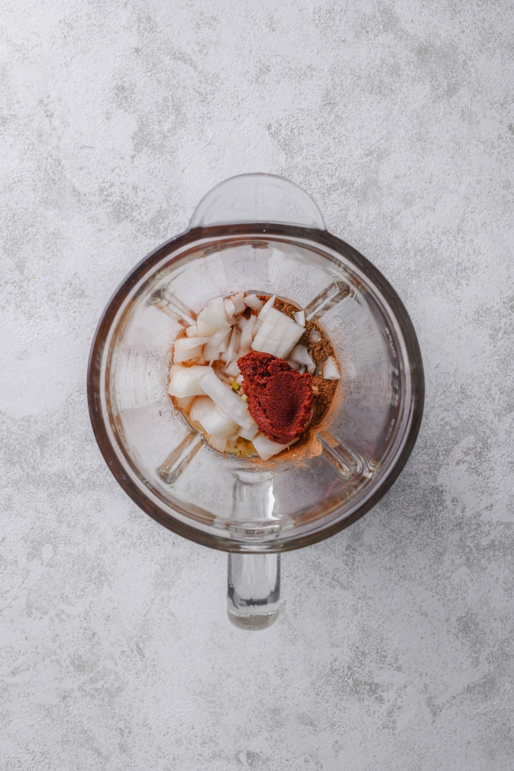 An overhead shot of a glass blender holding al pastor marinade ingredients including pineapple juice, chili powder, onion, and achiote paste.