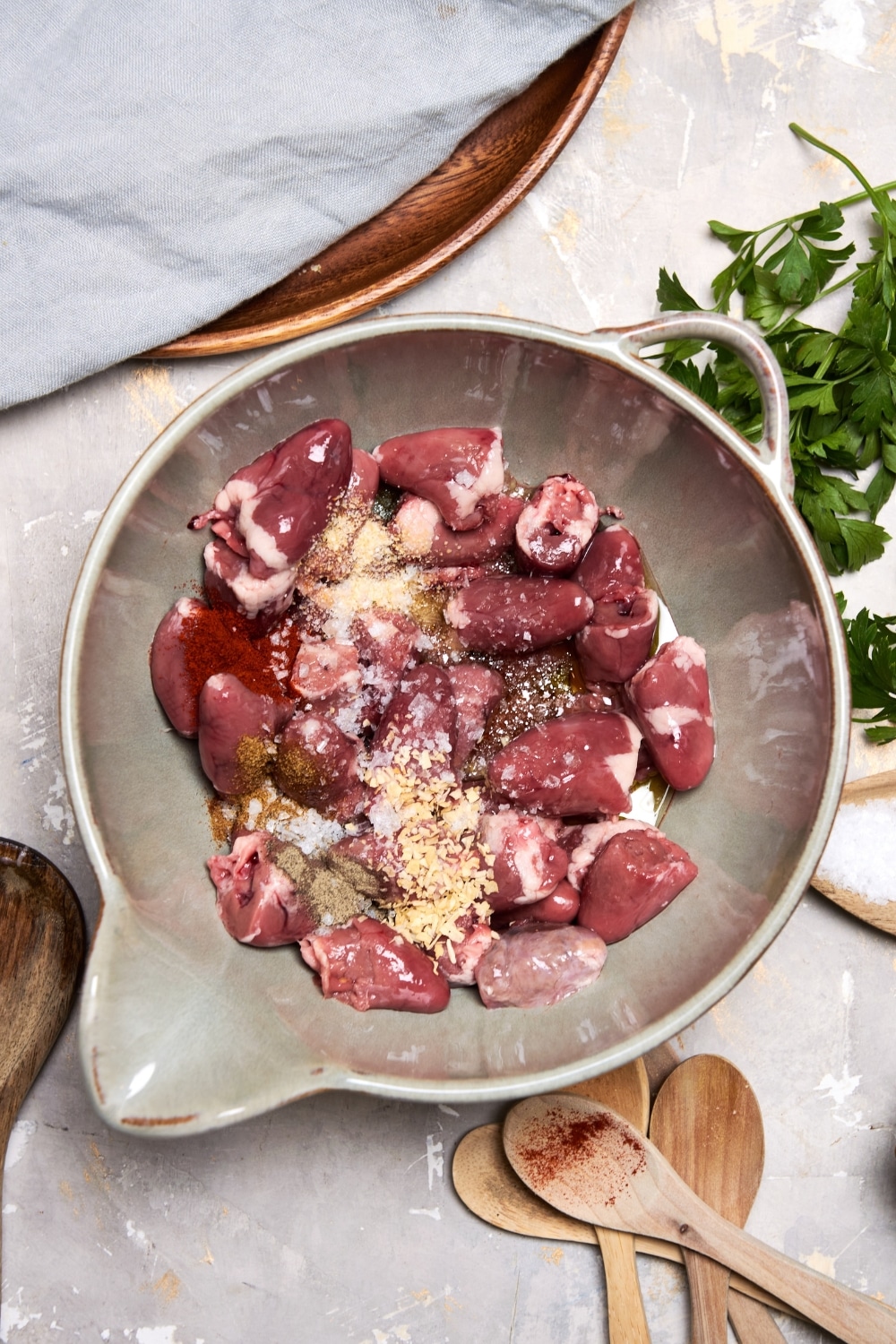 A ceramic mixing bowl filled with raw chicken hearts with seasonings on top such as salt and pepper, smoked paprika, garlic powder, and onion powder.
