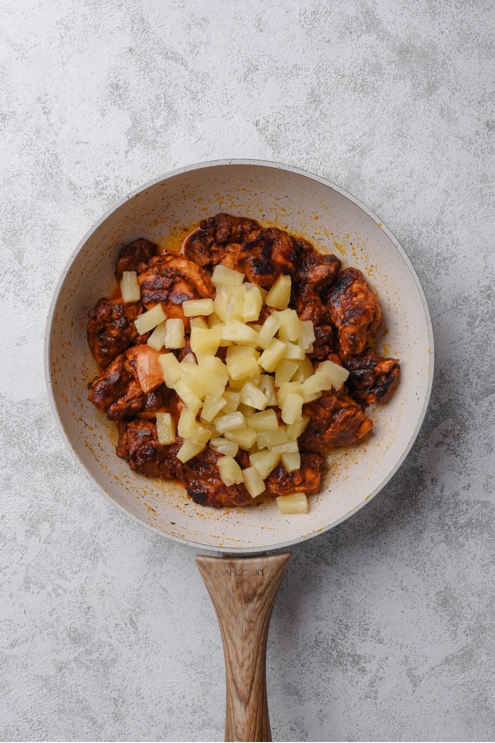 An overhead shot of a ceramic skillet with charred marinated chicken with fresh pineapple cooking on top.