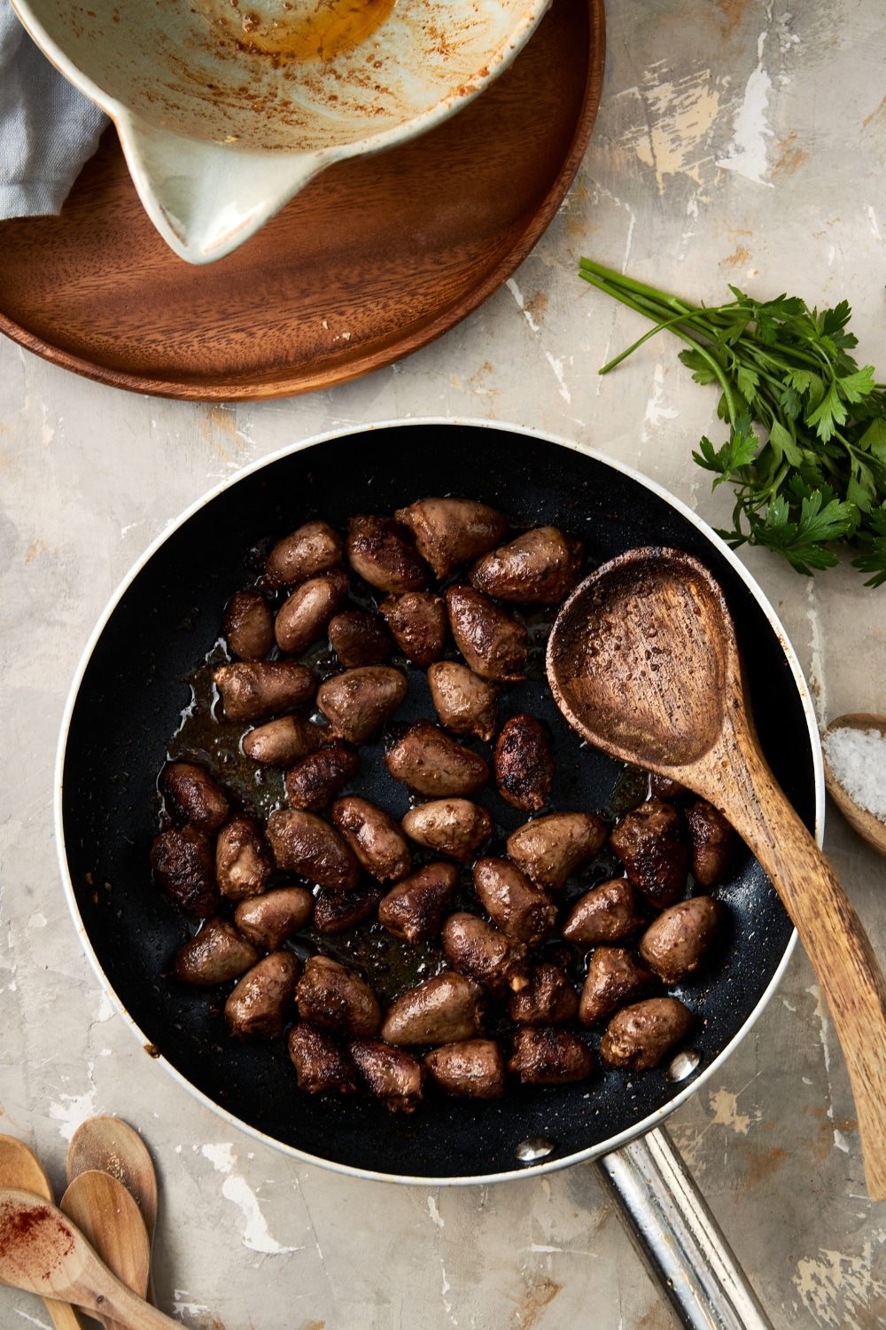 An overhead shot of a skillet with cooked chicken hearts and a wooden spoon resting in the skillet.