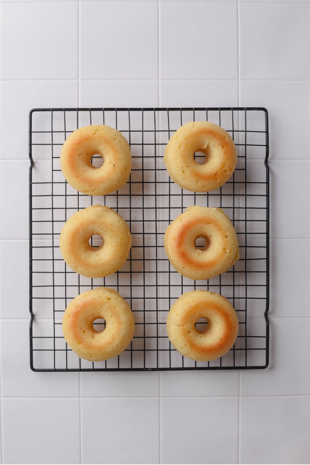 A wire rack with six baked donuts cooling on a tiled counter.