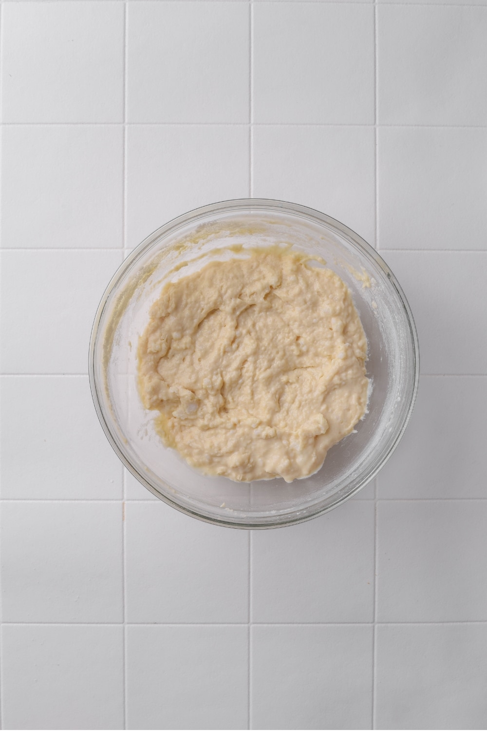 A glass bowl with donut batter on a tiled counter.