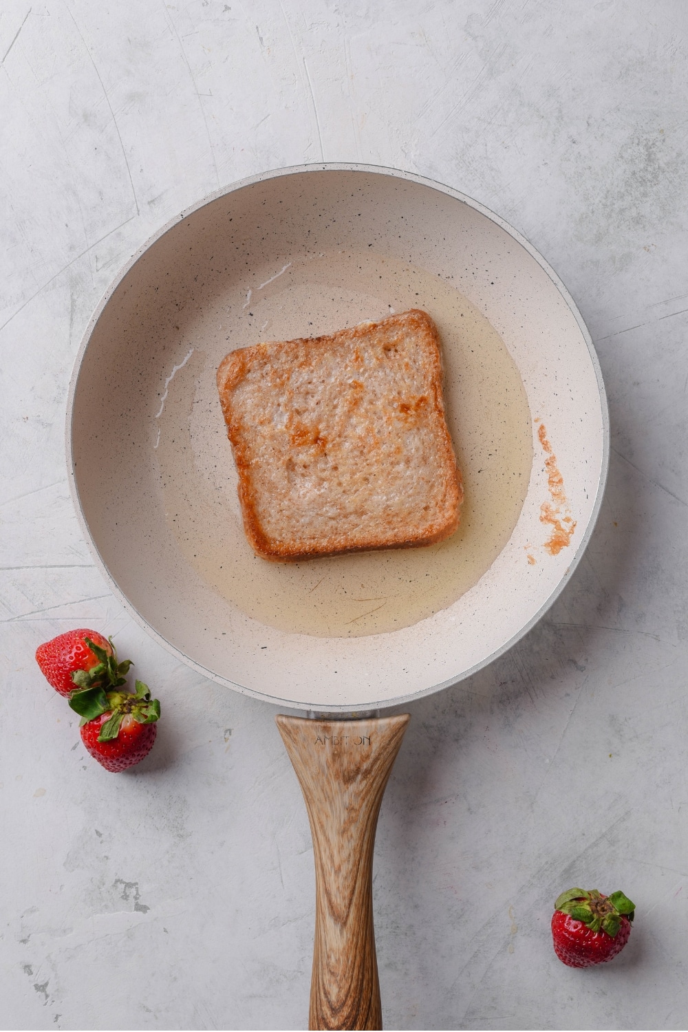 A slice of toast cooking on a ceramic pan with oil.