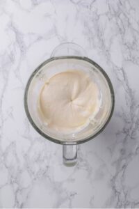 A glass blender blending a vanilla protein ice cream mixture.