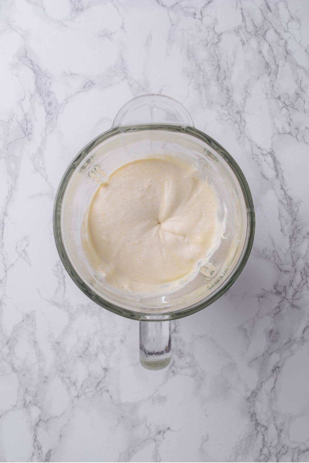 A glass blender blending a vanilla protein ice cream mixture.