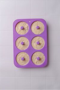 A silicone donut pan filled with raw donut batter on a tiled counter.